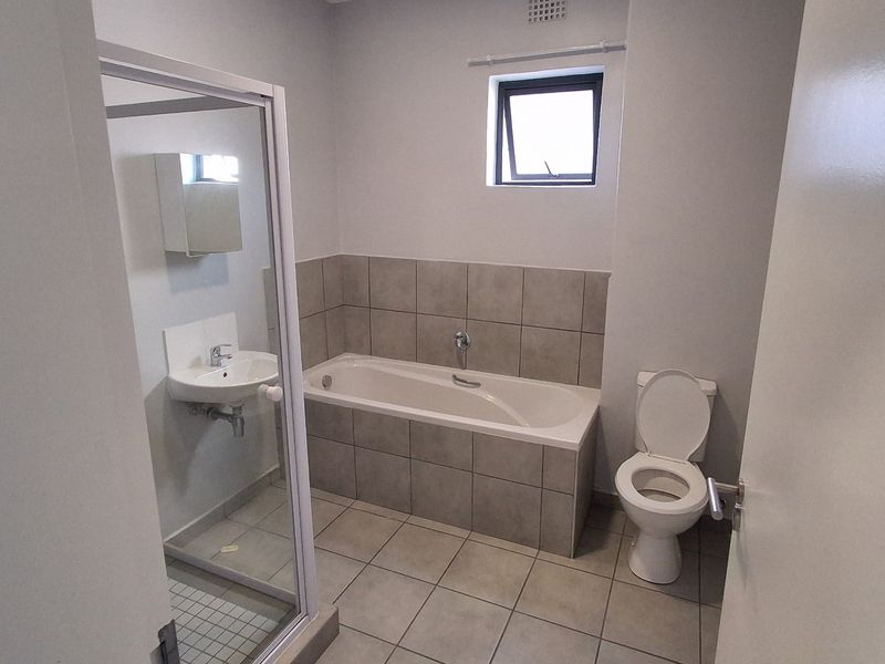 A clean, functional bathroom featuring a bathtub, separate shower enclosure, wall-mounted basin, and neutral floor-to-wall tiling.