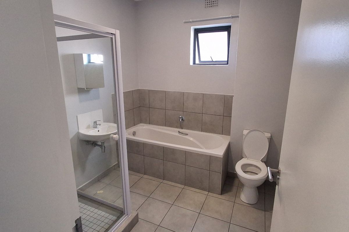 A clean, functional bathroom featuring a bathtub, separate shower enclosure, wall-mounted basin, and neutral floor-to-wall tiling.