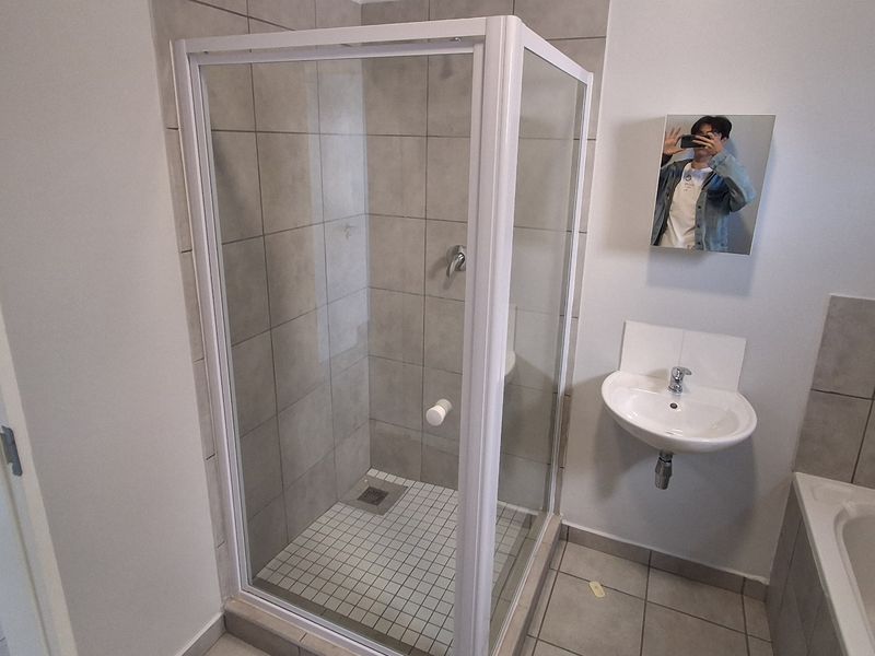 A clean, modern bathroom featuring a glass shower enclosure, wall-mounted basin, and a bathtub with neutral grey wall and floor tiling.