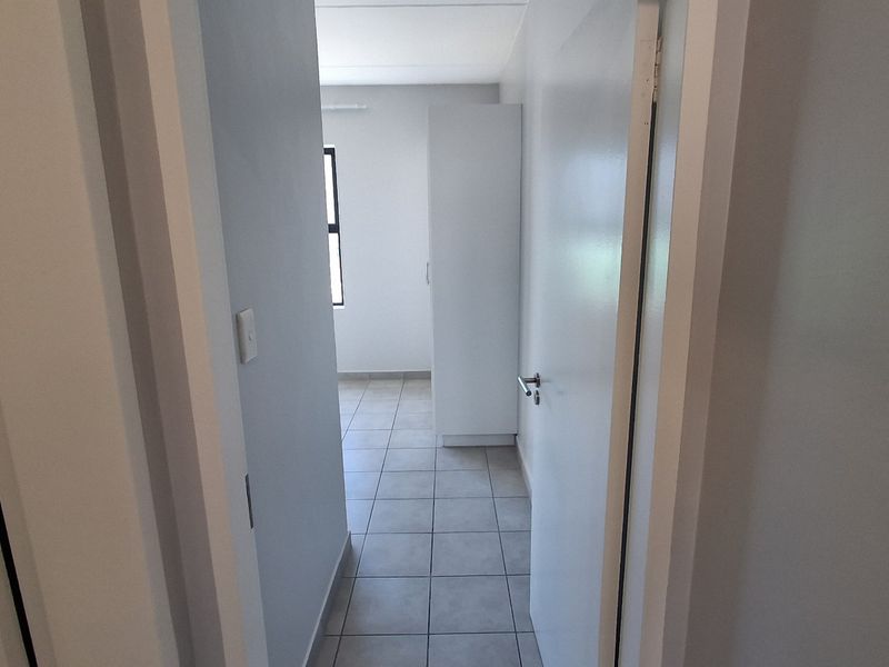 A clean, neutral hallway featuring tiled flooring and a built-in cupboard, providing a bright and functional transition space within the apartment.
