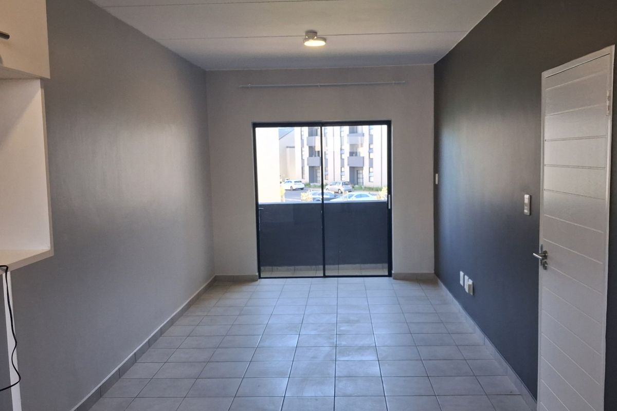 An empty, well-maintained living area featuring neutral tiled flooring, a sliding glass door leading to a balcony, and modern grey accent walls.