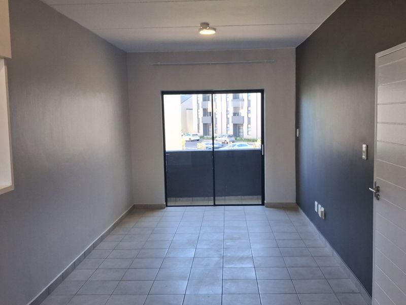 An empty, well-maintained living area featuring neutral tiled flooring, a sliding glass door leading to a balcony, and modern grey accent walls.