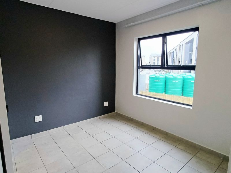 A clean, empty bedroom featuring neutral tiled flooring, a dark accent wall, and an aluminium-framed window with exterior views.