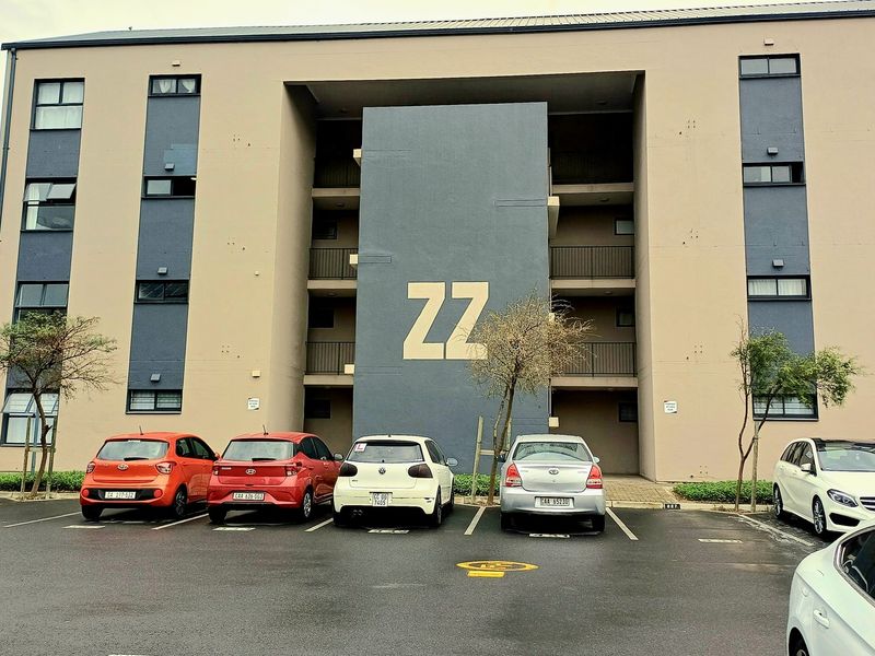 Front elevation of a multi-story apartment complex featuring a central stairwell and dedicated asphalt parking area.