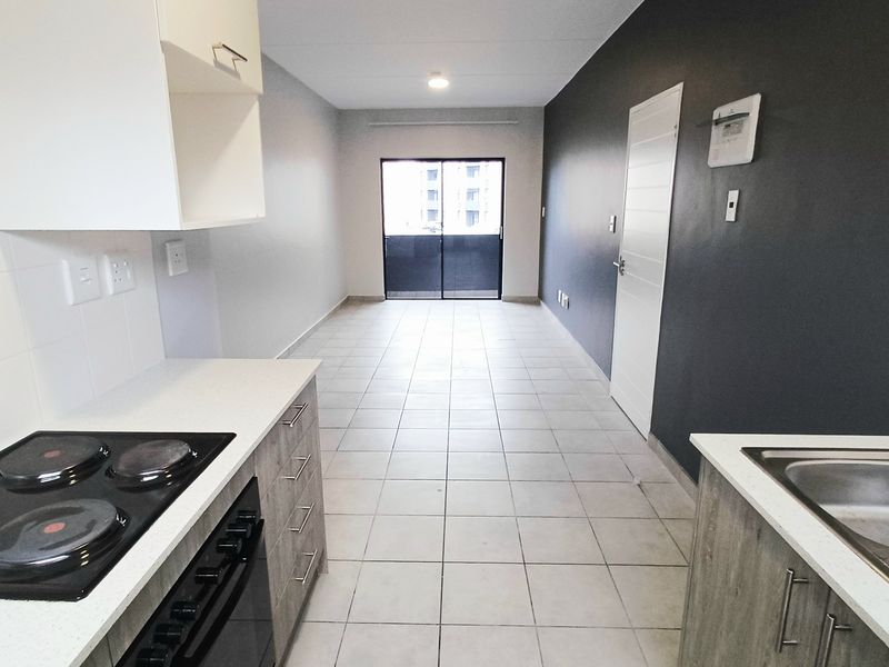 Open-plan kitchen and living area featuring tiled flooring, modern cabinetry, built-in oven and hob, and access to a balcony through sliding glass doors.