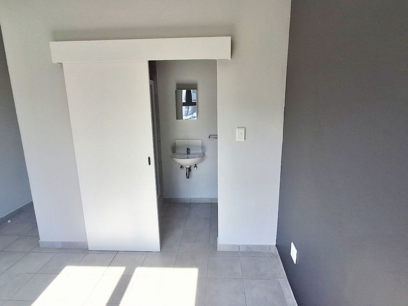 A clean, minimalist bathroom area featuring a wall-mounted basin, sliding door access, and neutral tiled flooring in a modern apartment setting.