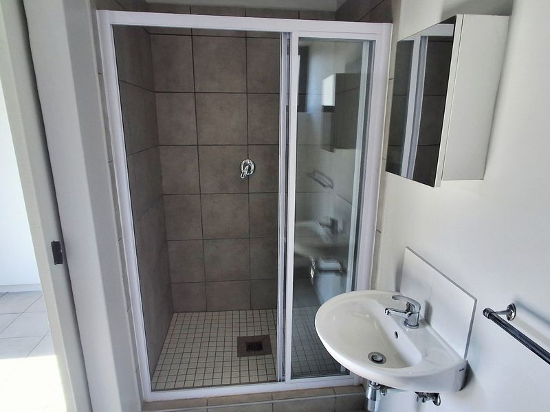 A clean, modern bathroom featuring a glass-enclosed shower with grey tiling, a wall-mounted basin, and a mirrored medicine cabinet.