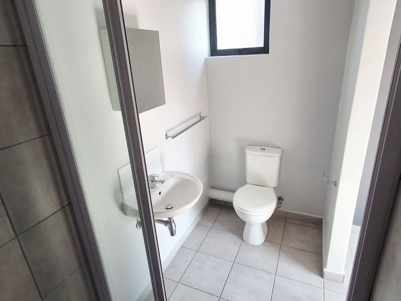 A clean, functional bathroom featuring a wall-mounted basin, toilet, and tiled flooring with neutral finishes.