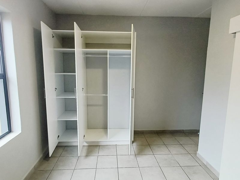 A bright, empty bedroom featuring neutral tiled flooring, a built-in wardrobe, and a large window providing natural light.