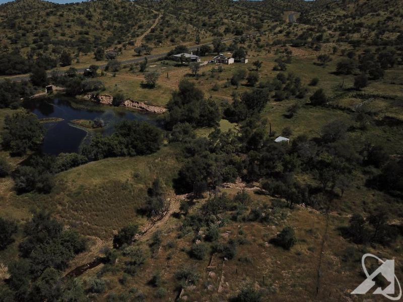 Aerial view of a large, undeveloped residential land parcel featuring natural vegetation, a water body, and existing perimeter fencing.
