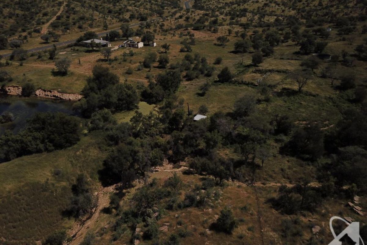 An aerial view of a large, undeveloped residential land parcel featuring natural vegetation, hilly terrain, and a small water body.
