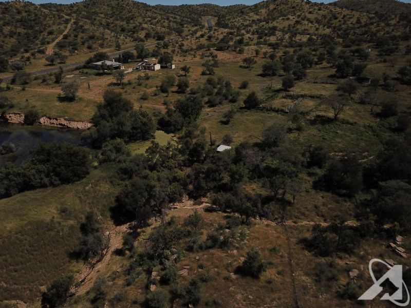An aerial view of a large, undeveloped residential land parcel featuring natural vegetation, hilly terrain, and a small water body.