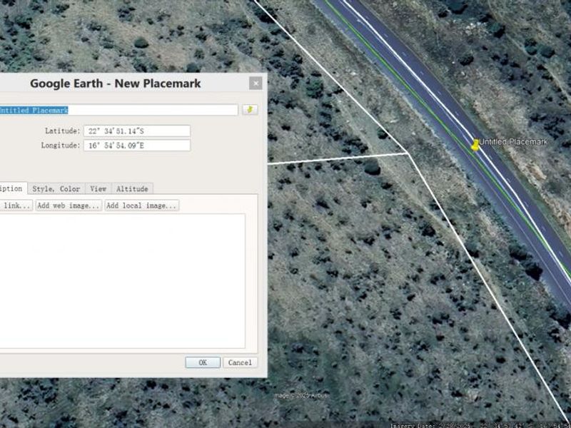 An aerial satellite view of a vacant land plot showing surrounding terrain and adjacent road access.