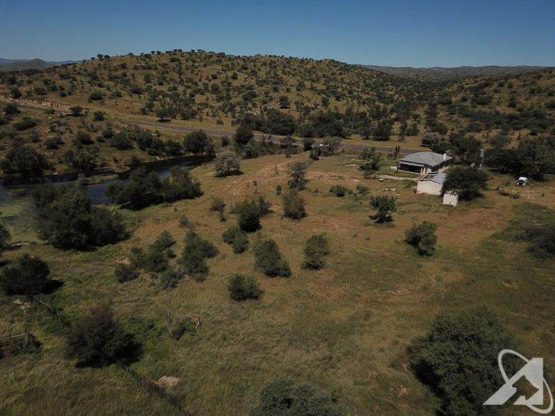 Aerial view of a large vacant residential land parcel featuring natural landscape, river frontage, and existing structures.
