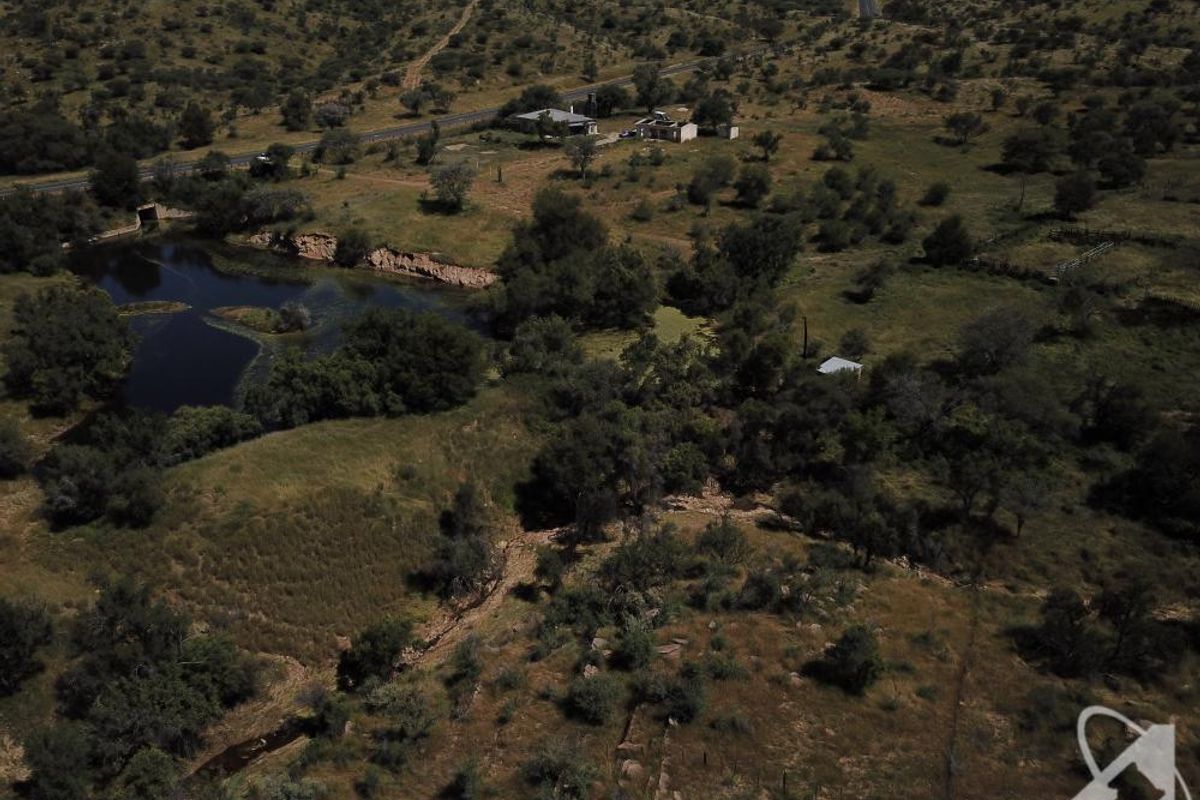 Aerial view of a large, undeveloped residential land parcel featuring natural vegetation, a water body, and existing perimeter fencing.