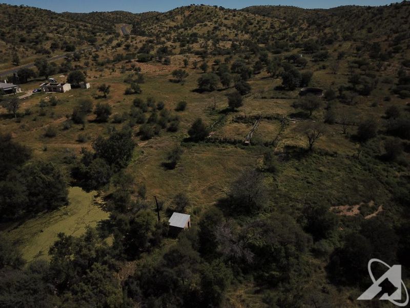 Aerial view of a large vacant residential plot featuring natural landscape, fencing, a water reservoir, and a small outbuilding.