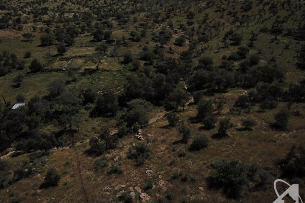 An aerial view of a large, undeveloped residential land plot featuring natural terrain, scattered trees, and existing perimeter fencing.