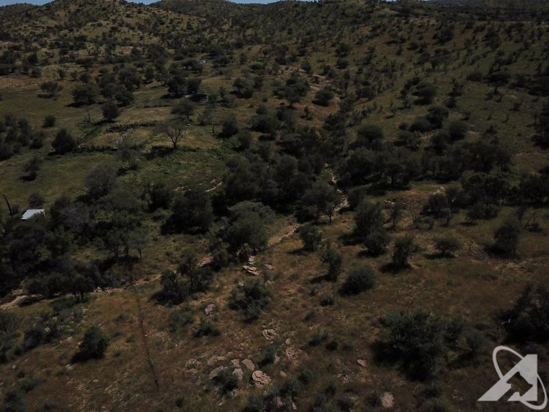 An aerial view of a large, undeveloped residential land plot featuring natural terrain, scattered trees, and existing perimeter fencing.