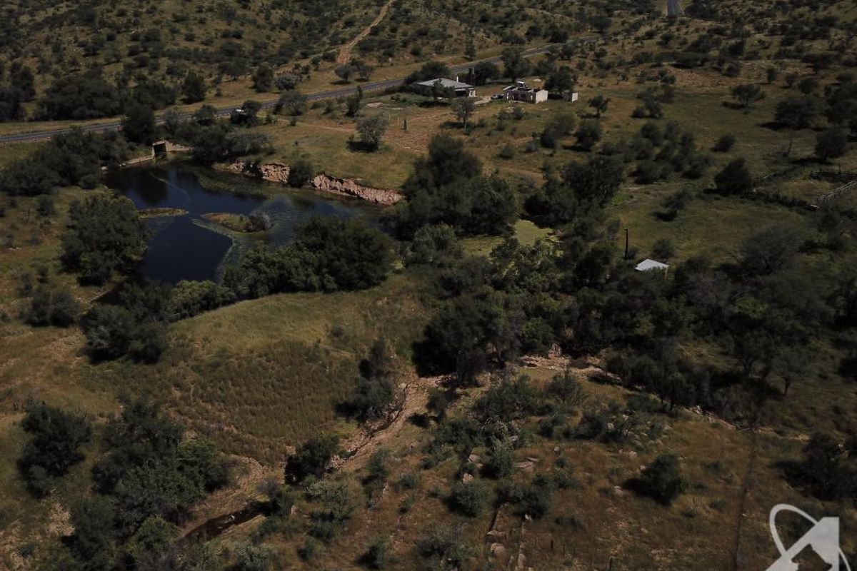 Aerial view of a large vacant residential land parcel featuring natural terrain, native vegetation, and a small water body.