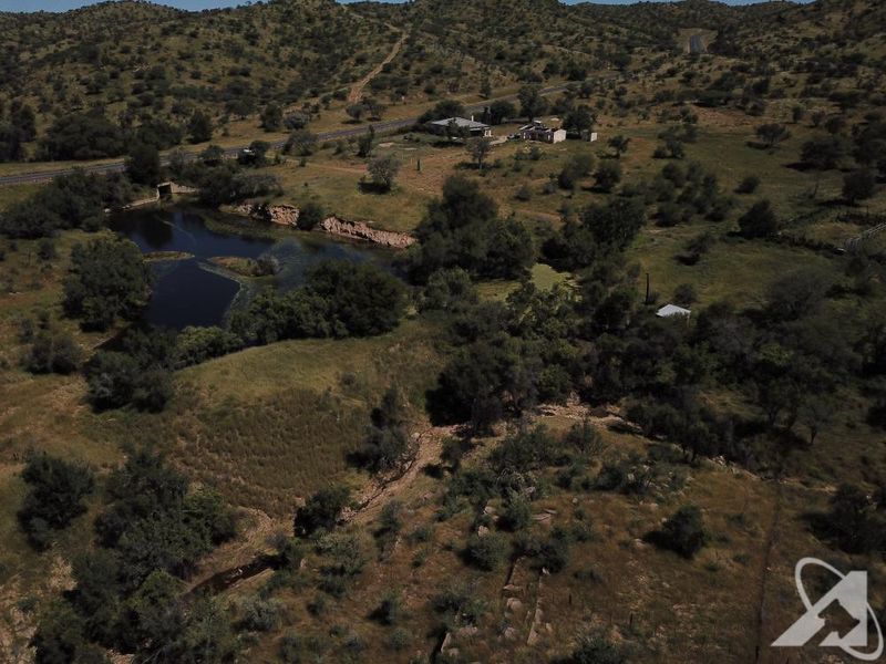 Aerial view of a large vacant residential land parcel featuring natural terrain, native vegetation, and a small water body.