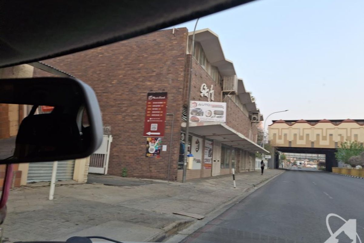 Street-level view of a commercial brick building with signage, captured from a vehicle.