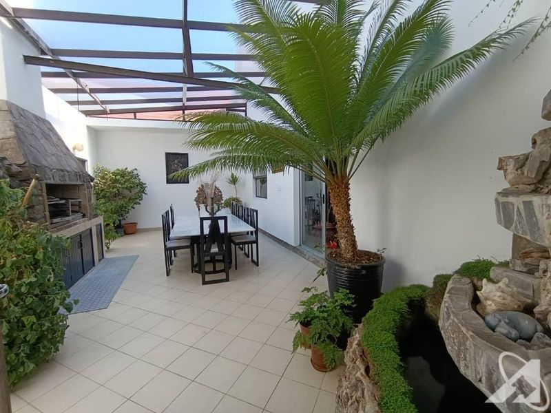 Covered outdoor patio featuring a built-in braai, tiled flooring, and a stone water feature, ideal for alfresco dining and entertaining.