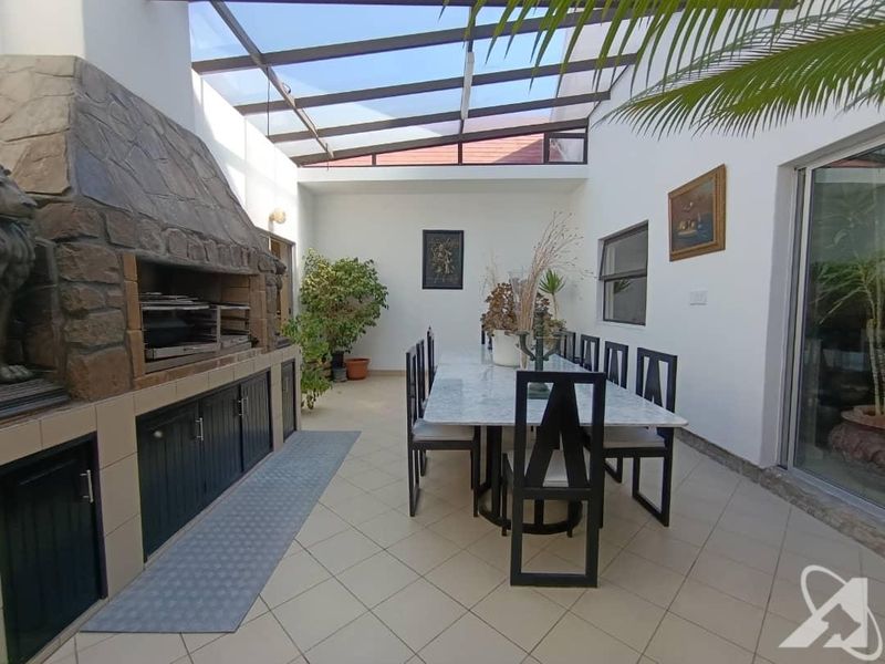 Covered patio area featuring a built-in stone braai, tiled flooring, and a translucent roof, providing a versatile space for outdoor dining and entertainment.
