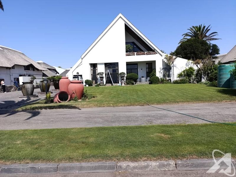 Front view of a modern A-frame house featuring a pitched roof, balcony, and a well-maintained lawn with a paved driveway.
