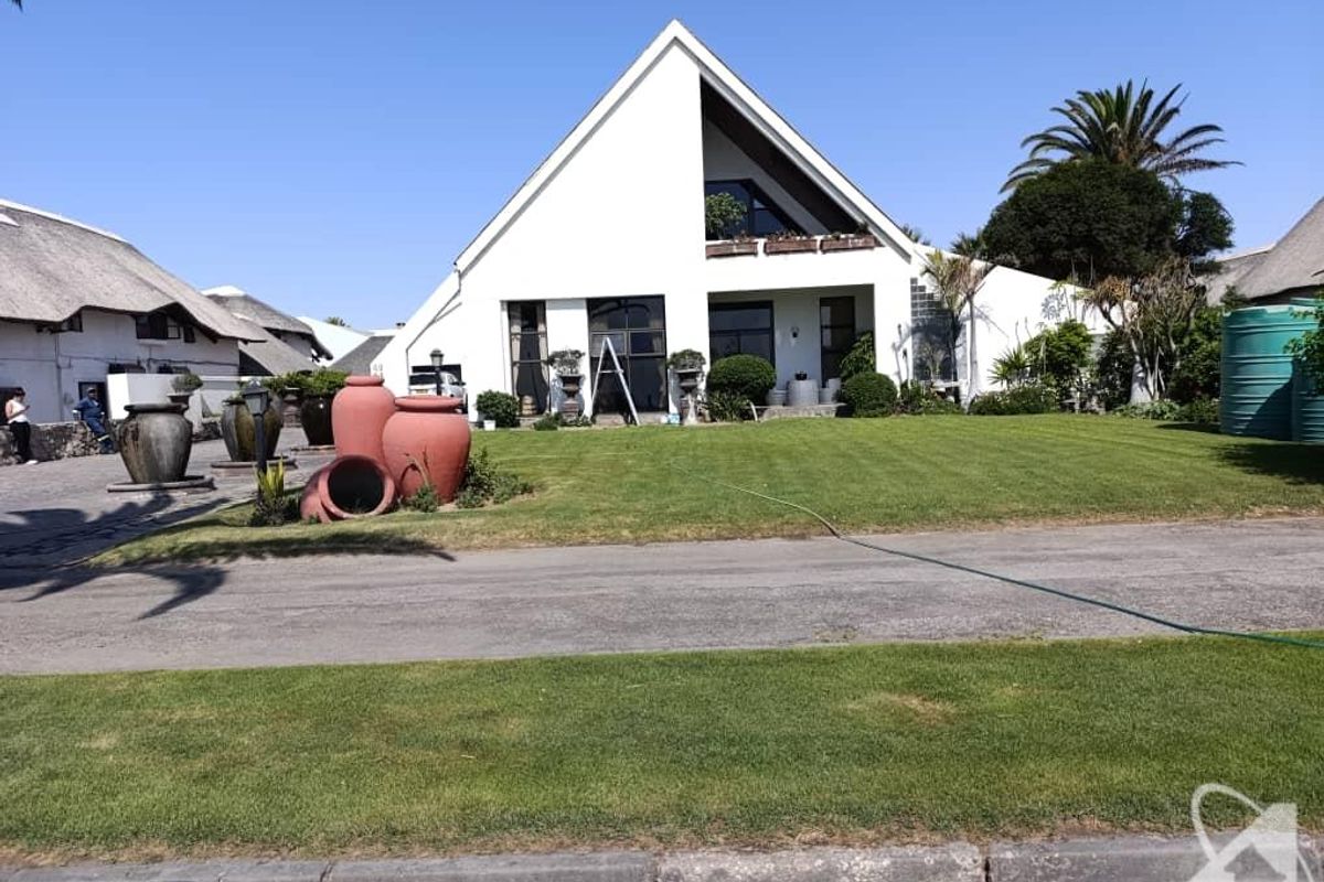Front view of a modern A-frame house featuring a pitched roof, balcony, and a well-maintained lawn with a paved driveway.