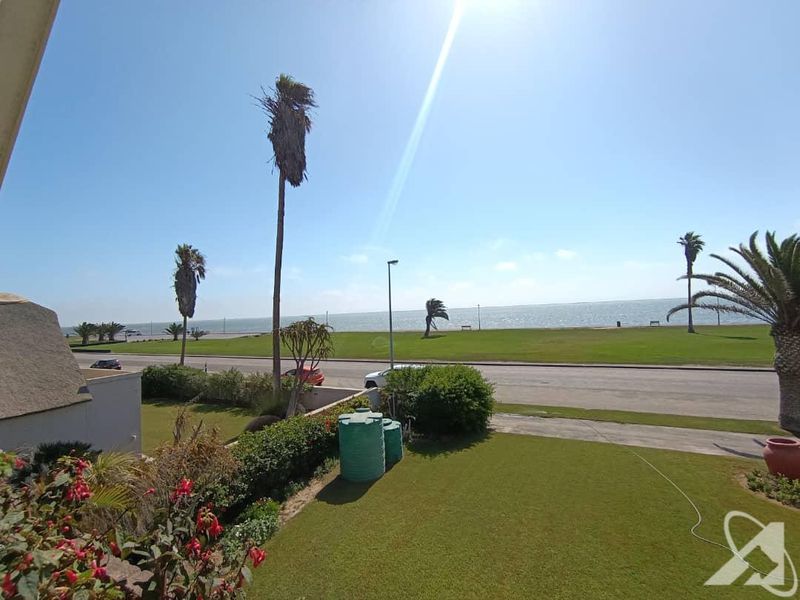 A scenic view overlooking a coastal road, green lawn, and the ocean, featuring well-maintained garden space and water storage tanks.