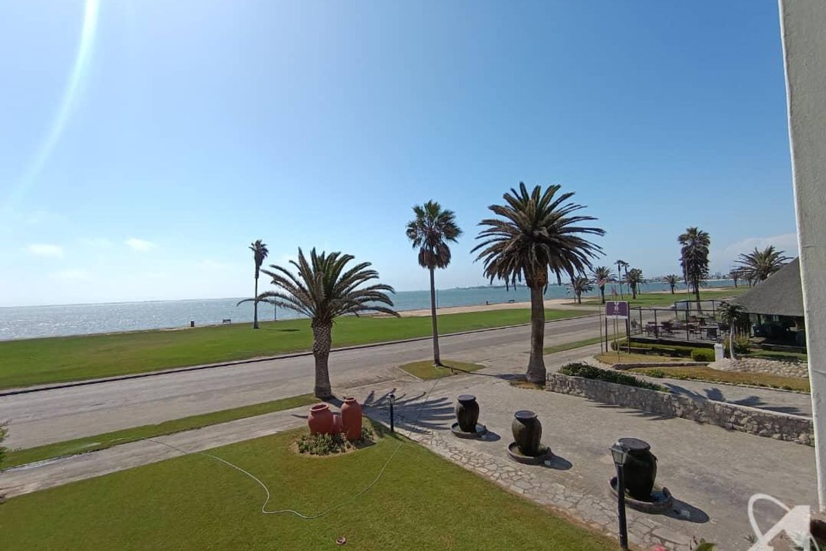Elevated view overlooking a manicured garden, paved driveway, and coastal road with scenic ocean vistas.