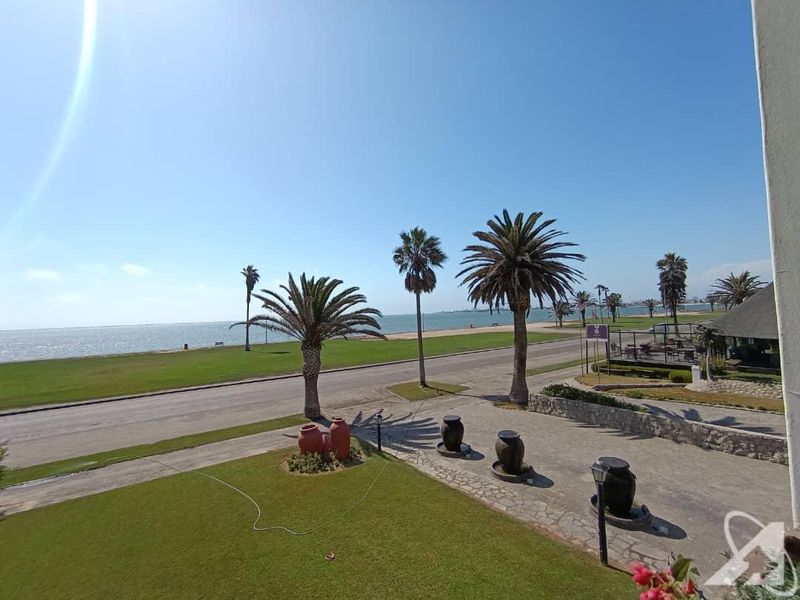 Elevated view overlooking a manicured garden, paved driveway, and coastal road with scenic ocean vistas.
