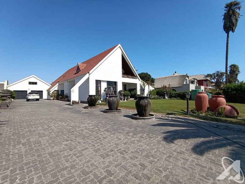 Spacious front exterior view featuring a large cobblestone driveway, well-maintained lawn, and a distinctive white house with a tiled roof and detached garage.