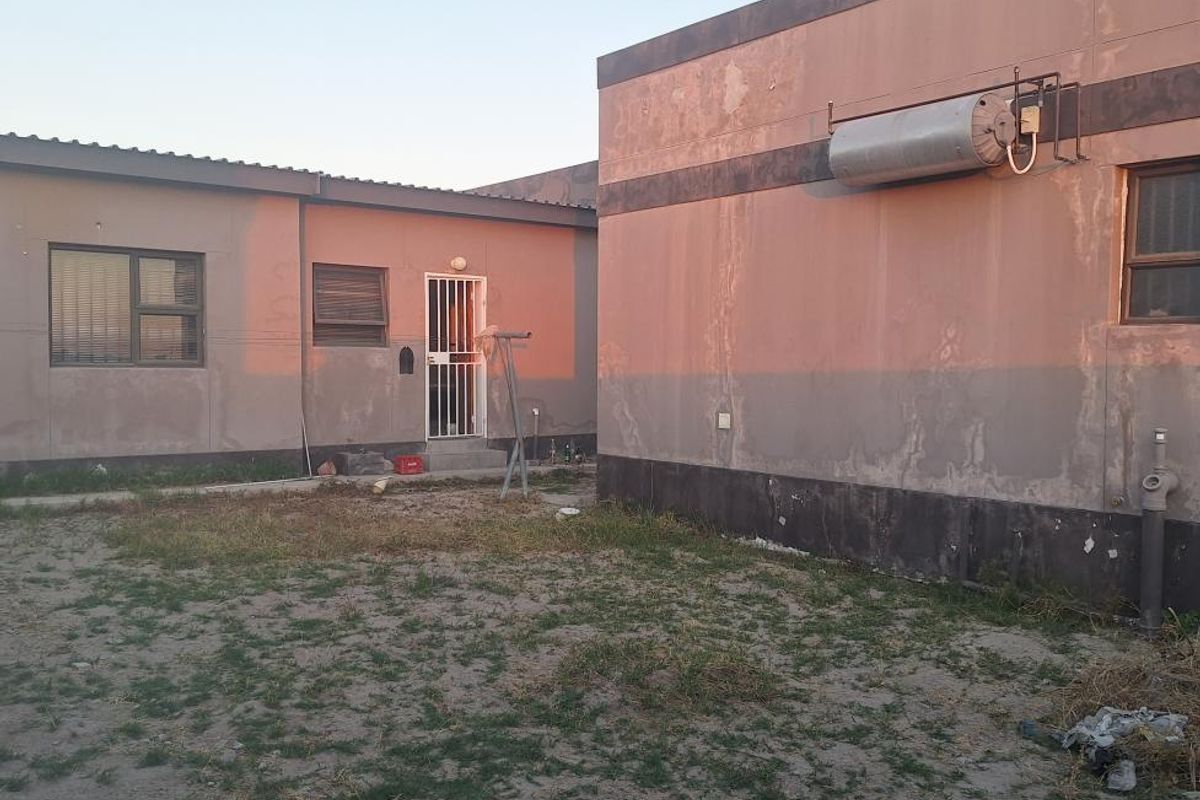 Rear exterior view of the property showing the building facade, solar geyser installation, and surrounding yard area.
