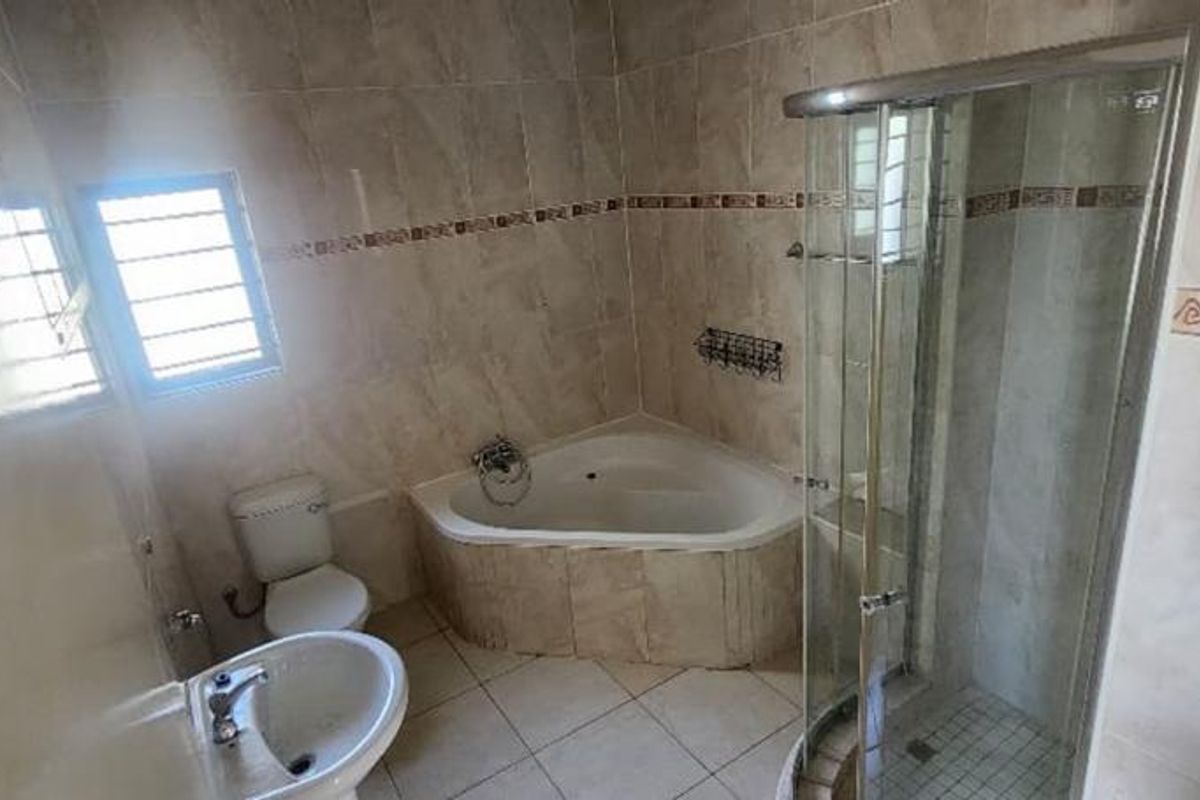 A functional bathroom featuring a corner bathtub, a separate glass-enclosed shower, a pedestal basin, and a toilet with neutral wall and floor tiling.