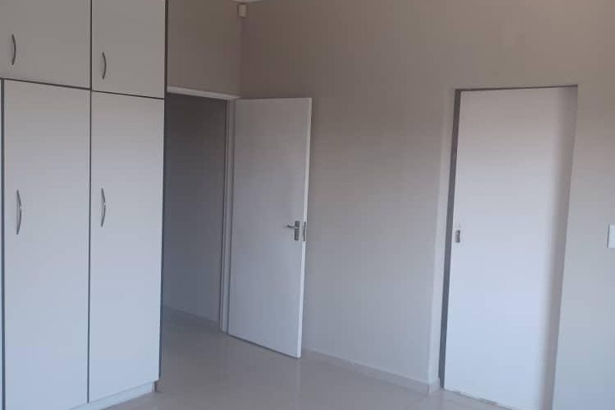 A clean, empty bedroom featuring neutral tiled flooring, built-in white cabinetry, and simple interior doors.