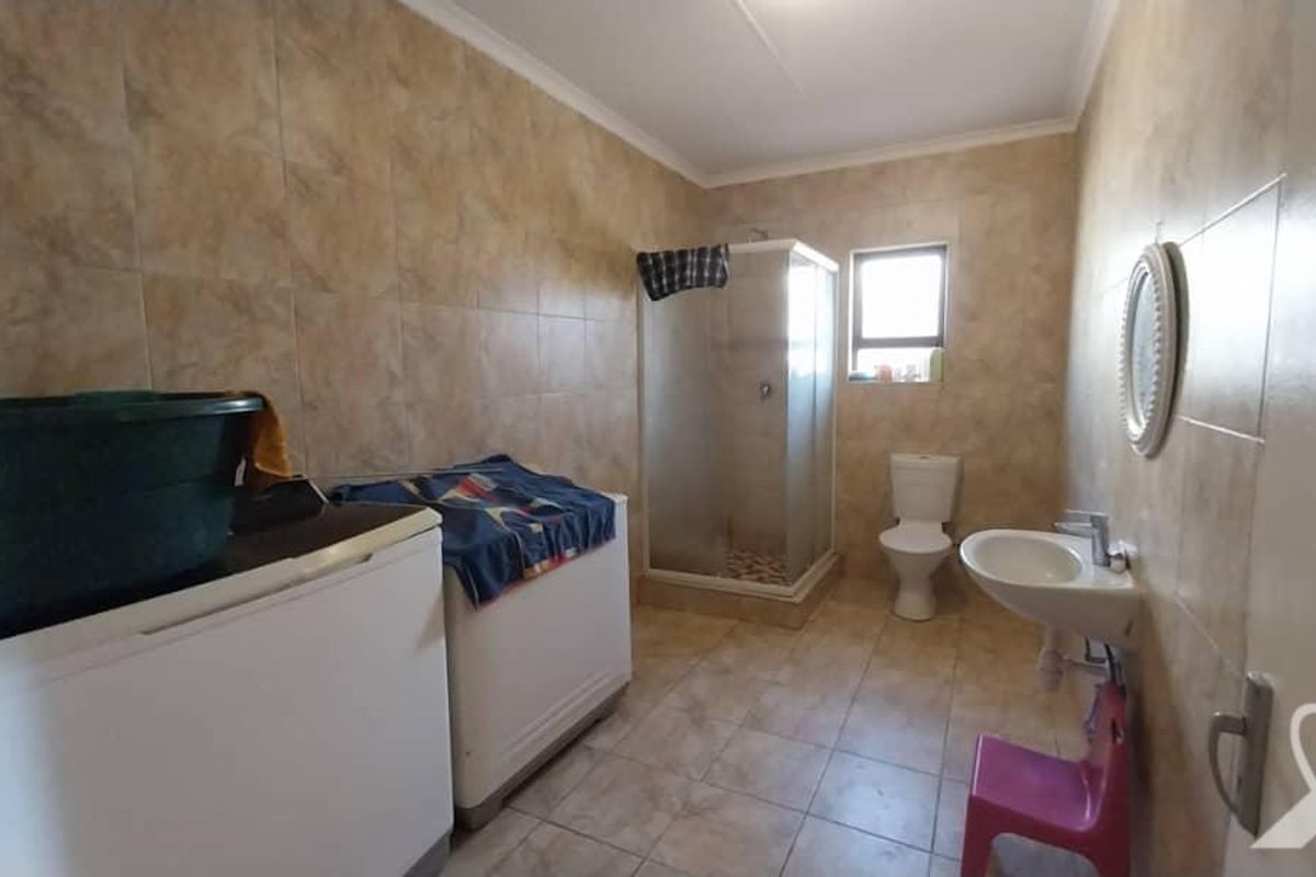 A functional bathroom featuring a shower enclosure, toilet, and wall-mounted basin, finished with neutral wall and floor tiling.