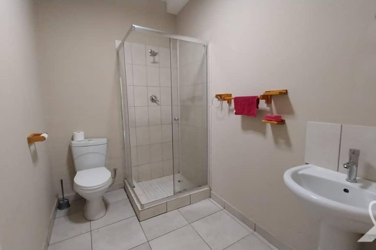 A functional bathroom featuring a glass-enclosed shower, pedestal basin, and toilet with neutral floor and wall tiling.