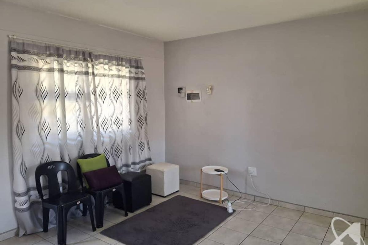 A simple living area featuring tiled flooring, a large window with curtains, and wall-mounted electrical distribution board.
