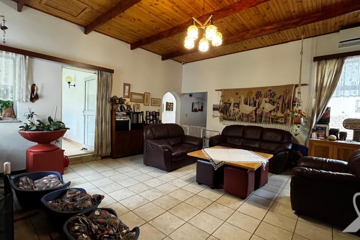 Spacious living room featuring exposed timber beam ceilings, tiled flooring, and a split-system air conditioning unit.