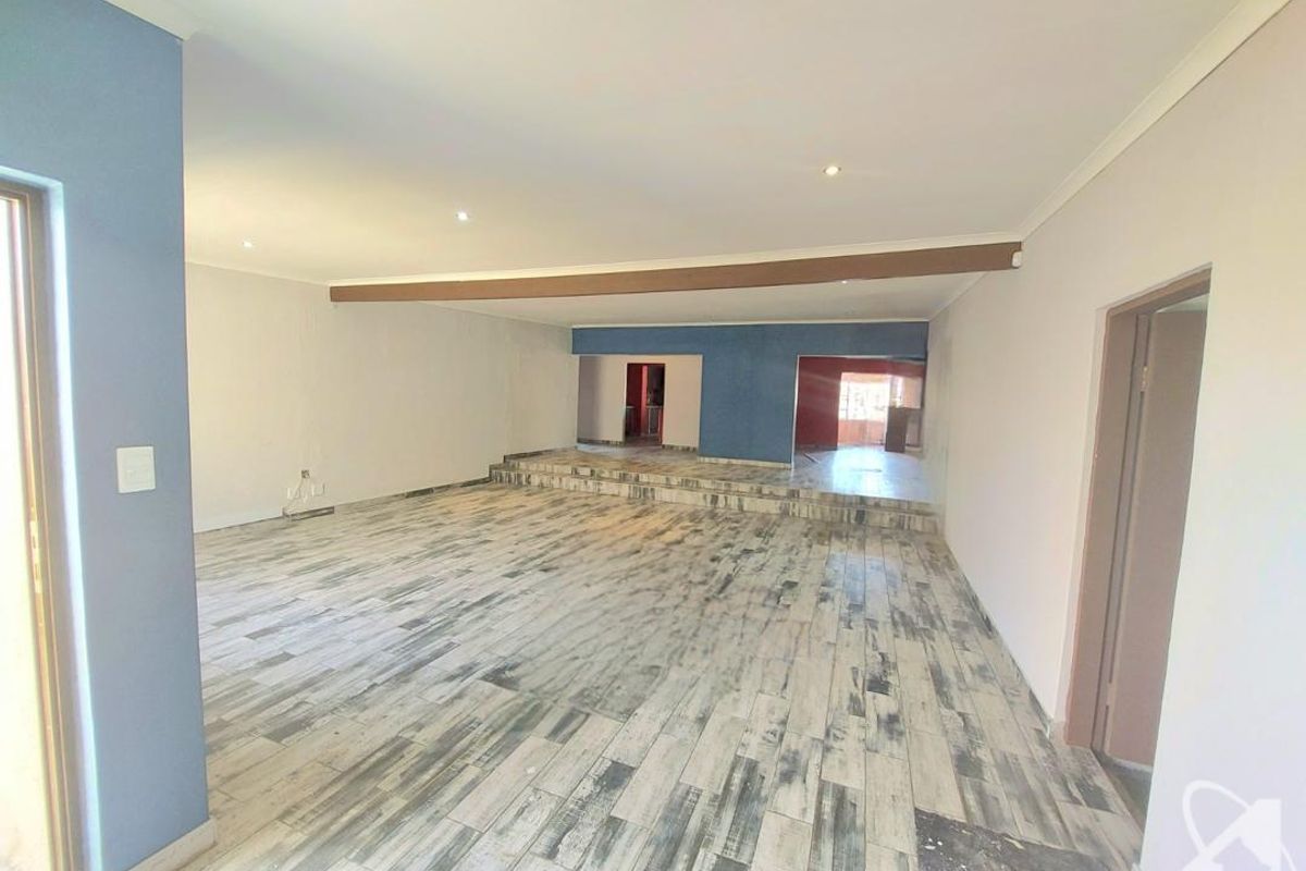 Spacious, empty living area featuring a raised platform, wood-look tiled flooring, and recessed downlighting, offering a versatile open-plan layout.