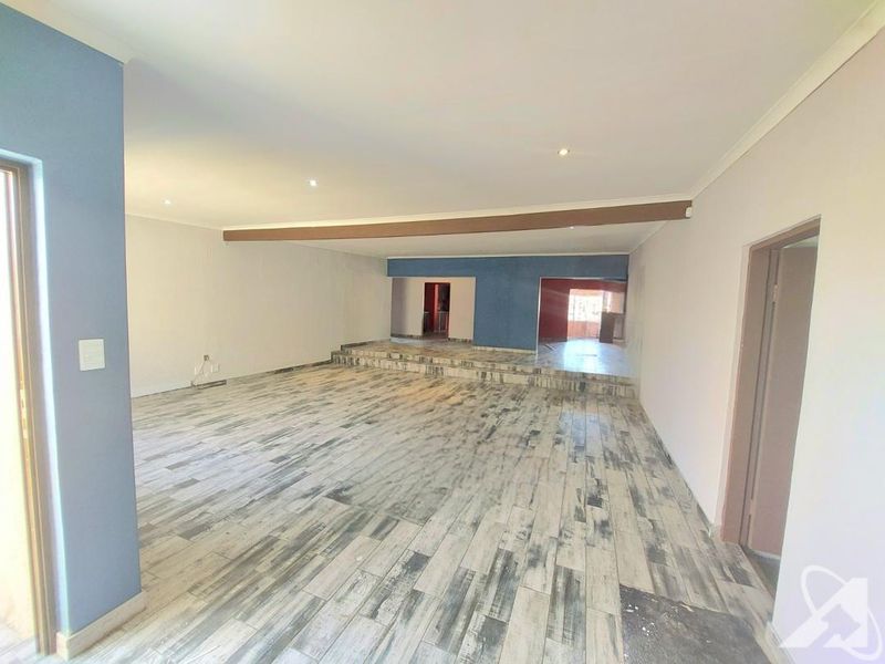 Spacious, empty living area featuring a raised platform, wood-look tiled flooring, and recessed downlighting, offering a versatile open-plan layout.