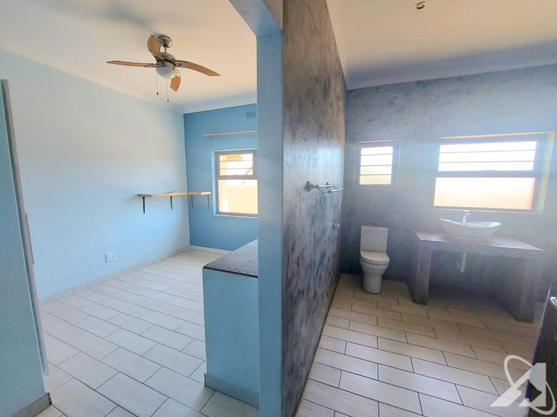 An open-plan bedroom featuring an integrated en-suite bathroom with a concrete vanity, vessel sink, and tiled flooring throughout.
