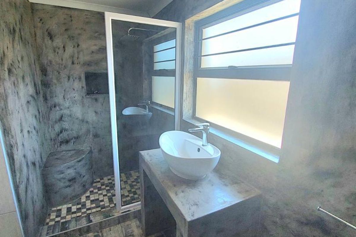 Modern bathroom featuring a concrete vanity with a vessel sink, walk-in shower with a built-in bench, and textured tiled flooring.