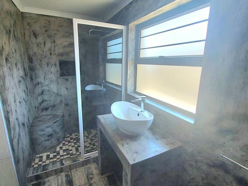 Modern bathroom featuring a concrete vanity with a vessel sink, walk-in shower with a built-in bench, and textured tiled flooring.