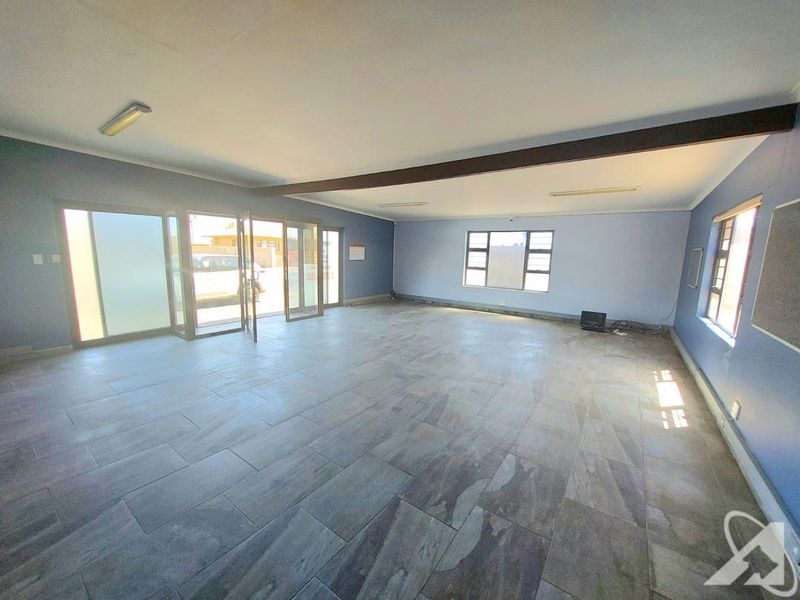 A spacious, empty living area featuring large format floor tiles, aluminium sliding doors, and natural light from multiple windows.