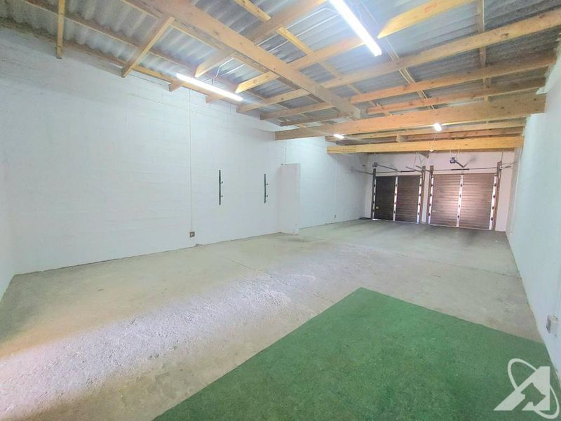 A spacious, unfinished double garage featuring exposed timber rafters, concrete flooring, and dual garage doors, offering significant potential for storage or workshop use.