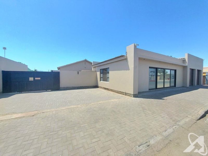 Front exterior view of the property featuring a paved driveway, perimeter wall, security gate, and modern sliding glass entrance doors.
