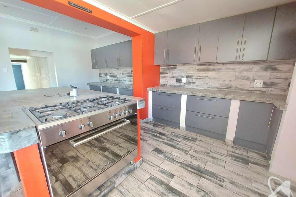 Modern kitchen featuring grey cabinetry, stone countertops, a gas stove, and wood-look tiled flooring with a bold orange accent wall.