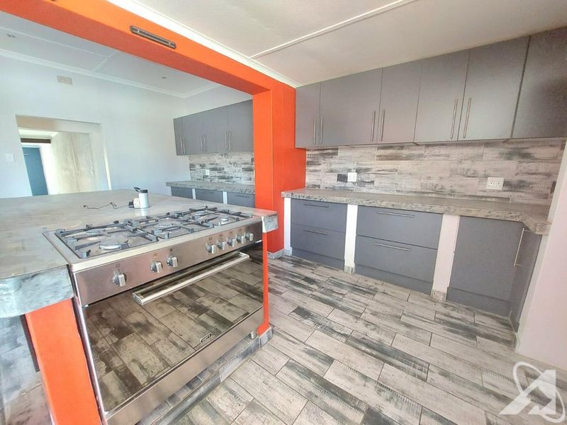 Modern kitchen featuring grey cabinetry, stone countertops, a gas stove, and wood-look tiled flooring with a bold orange accent wall.